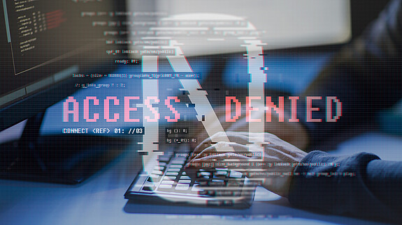 Cybersolidarität Nahaufnahme eines Hackers, der in einem abgedunkelten Raum vor zwei Monitoren sitzt und über die Tastatur versucht, in ein System einzudringen.