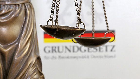 Nahaufnahme einer Justitia vor dem deutschen Grundgesetzbuch