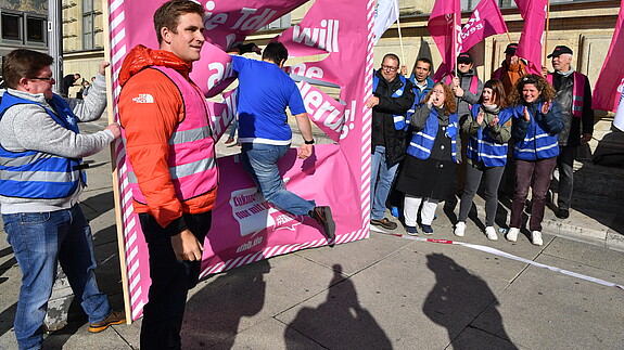 Prozentlauf München Mann springt durch ein Papier-Plakat. Um ihn herum stehen zahlreiche Demonstrierende und feuern ihn an.
