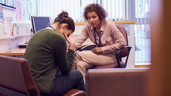 Psychische Belastung im Dienst: Gesundheitsprävention umfasst mehr als einen ergonomischen Arbeitsplatz Junge Frau im Gespräch mit einer weiblichen Vertrauensperson über psychische Belastungen