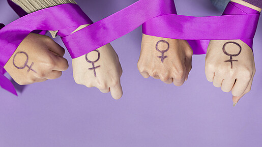 Vier Frauenhände mit einem aufgemalten Frauen-Symbol, ein violettes Band ist um die Handgelenke gelegt