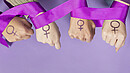 Vier Frauenhände mit einem aufgemalten Frauen-Symbol, ein violettes Band ist um die Handgelenke gelegt
