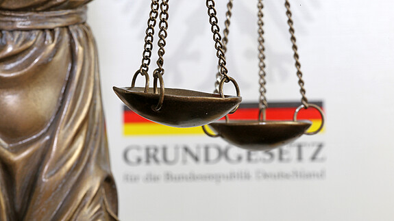 Nahaufnahme einer Justitia vor dem deutschen Grundgesetzbuch