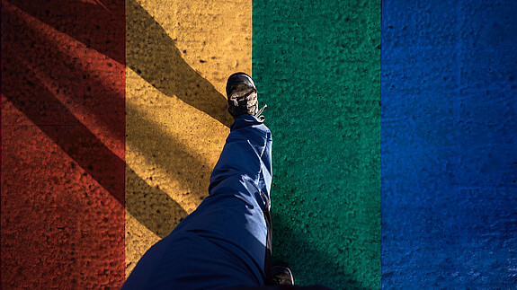 Eine Person geht über eine asphaltierte Straße, die in den Regenbogenfarben angemalt ist.