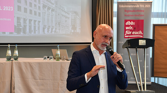 Regionalkonferenz in Düsseldorf Ein Mann steht vor einer Leinwand mit einem Mikrofon in der Hand