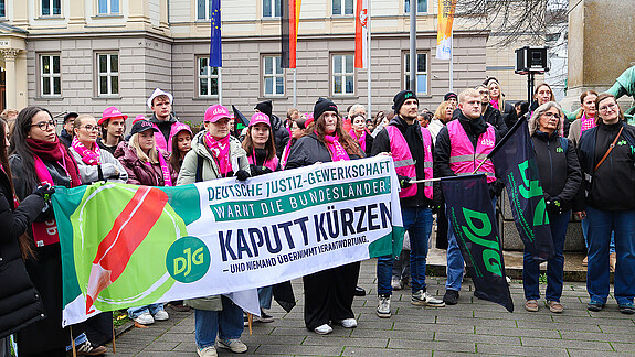 Eine Gruppe Menschen demonstriert mit Bunten Bannern und Warnwesten auf einem Platz.