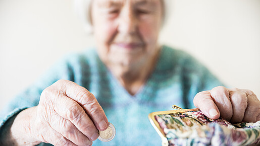 Eine unglücklich wirkende Seniorin zählt am Tisch die wenigen Münzen ihre Pension.