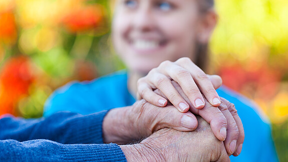 Soziale Arbeit aufwerten Junge Frau legt Hand auf die Hand eines Senioren