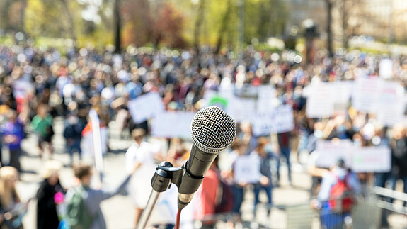 Protest or public demonstration, focus on microphone, blurred group of people in the background protest, demonstration, people, group, crowd, banner, microphone, protester, political, social, democracy, anti-racism, strike, street, movement, politic, rally, audience, speaker, public, auditorium, mass, event, right, human, orator, civil, unrecognizable, activism, justice, election, meeting, labor, nonviolent, convention, resistance, climate, covid-19, lockdown, coronavirus, pandemic, resist, politics, protesters, rights, recording, presentation, demonstrations