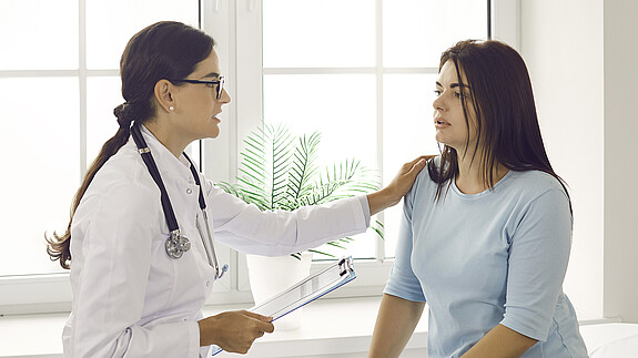 Hemsing: „Pflege braucht Qualität und Qualität braucht Fachkräfte!“ Doctor talking to patient, comforting, supporting and reassuring her. Worried young woman having conversation with physician about health issues while sitting in exam room in modern clinic or hospital