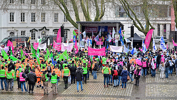 Eine Menschengruppe protestiert mit bunten Fahnen auf einem öffentlichen Platz.
