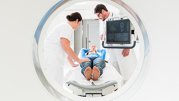 Doctor, nurse, and patient at CT scan Doctor, physician, nurse, medical, specialist, radiology, radiologist, man, woman, Patient, hospital, clinic, medical team, Team, Teamwork, working, MRI, MRT, CT, computer tomography, imaging, magnetic resonance imaging, tomography, tomograph, x-ray, equipment, tube, scan, CT scan, Diagnostics, diagnose, screen, explaining, showing, care, health, healthcare, disease, medicine, people, staff, professionals, occupation, Caucasian, adult, standing, confident, white, young, competent