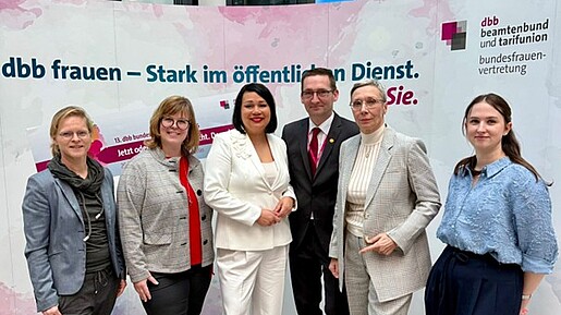 fünf frauen und ein Mann stehen vor einem rosa Aufsteller
